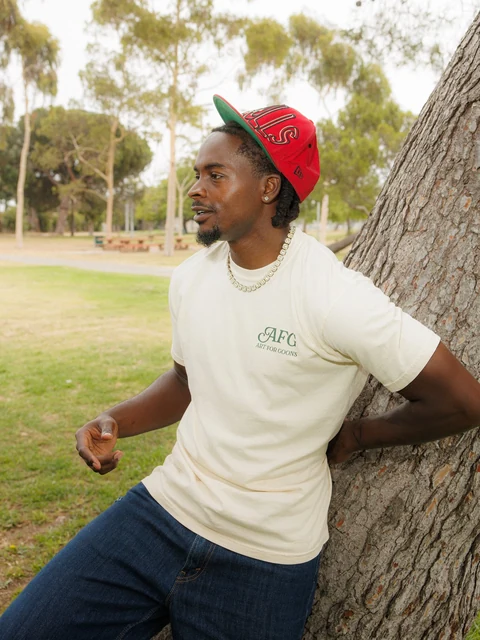 DK in the cream tee and a cap, leaning back