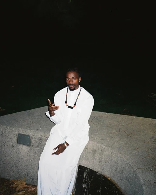 DK in a white robe, seated on a wall at night