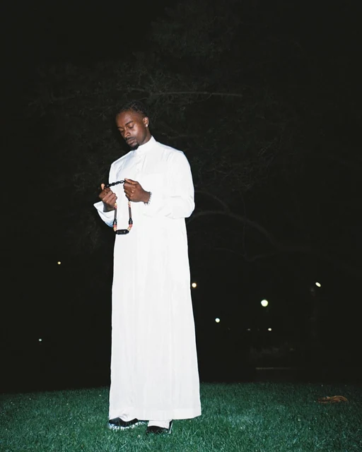 DK in a white robe standing on grass at night